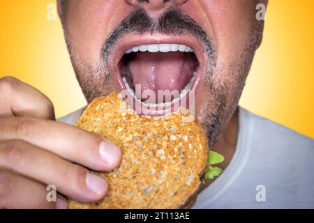 Irresistibile desiderio di cibo spazzatura. Primo piano di un uomo affamato che morde un brindisi al formaggio. Foto Stock