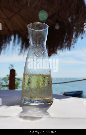 Acqua di frutta fresca in una caraffa di vetro sul tavolo nel ristorante sulla riva del mare. Limonata ghiacciata in spiaggia. Dettaglio della bottiglia. Gocce di W. Foto Stock