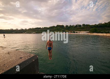 il bambino di 8 anni si tuffa in mare da un molo. Caldo giorno d'estate. Foto Stock