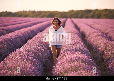 Giovane donna in camicia bianca nello splendido campo di lavanda al tramonto Foto Stock