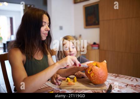 Famiglia felice che si prepara per Halloween. Madre e ragazzo intagliano la zucca a casa. Foto Stock