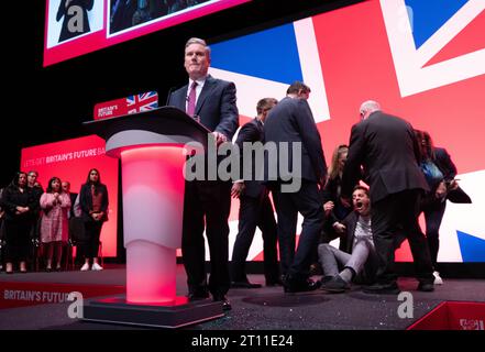 Liverpool, Regno Unito. 10 ottobre 2023. Il manifestante copre Keir Starmer con glitter durante l'inizio del discorso dei leader. Il manifestante è stato combattuto a terra e rimosso dalla sicurezza. Sir Keir si spazzolò i capelli si tolse la giacca e proseguì col discorso. Conferenza del lavoro 2023. Foto: Garyroberts/worldwidefeatures.com credito: GaryRobertsphotography/Alamy Live News Foto Stock