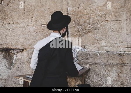 Giovane ebreo religioso in piedi contro il muro del pianto con un libro sacro e pregando. Gerusalemme, Israele: 24 ottobre 2018 Foto Stock