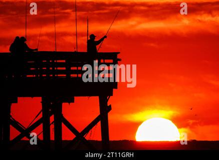 Isola di Palms, Stati Uniti. 10 ottobre 2023. Il folklore dei pescatori si staglia all'alba mentre scendono per la mattina al largo del molo Sea Cabins in una mattinata fredda nella bassa campagna, il 10 ottobre 2023 a Isle of Palms, South Carolina. Crediti: Richard Ellis/Richard Ellis/Alamy Live News Foto Stock