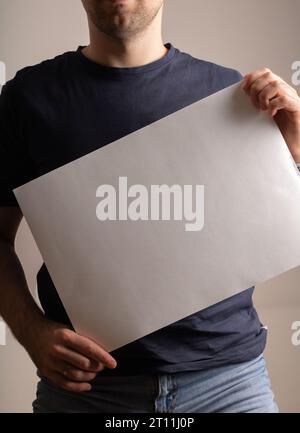 foto un uomo sta tenendo in mano un foglio bianco di carta, che mostra uno spazio vuoto per le informazioni. Il display simile a un poster attende il testo, un quadro per Convey Foto Stock
