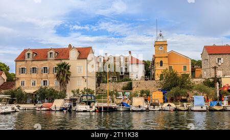 le piccole barche sono allineate sul molo del pittoresco porto di zlarin di fronte alla torre dell'orologio giallo chiamata leroj Foto Stock