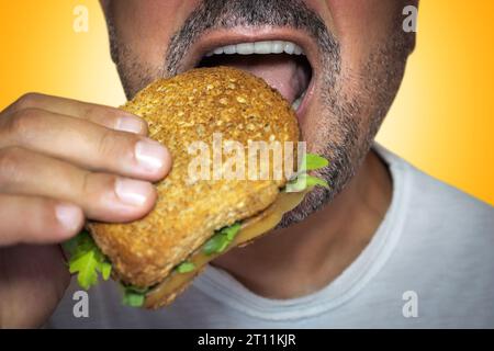 Irresistibile desiderio di cibo spazzatura. Primo piano di un uomo affamato che morde un brindisi al formaggio. Foto Stock