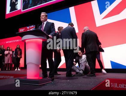 Il manifestante ha lottato a terra dalla sicurezza dopo aver coperto Keir Starmer con glitter durante l'inizio del discorso dei leader. Il manifestante è stato lottato a terra e rimosso dalla sicurezza. Sir Keir si spazzolò i capelli si tolse la giacca e proseguì col discorso. Conferenza del lavoro 2023. Immagine: Garyroberts/worldwidefeatures.com Foto Stock