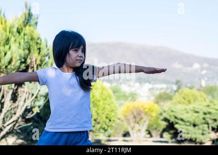 Bambina che fa esercizi in un bellissimo parco con colori verdi accesi e montagne sullo sfondo. Foto Stock