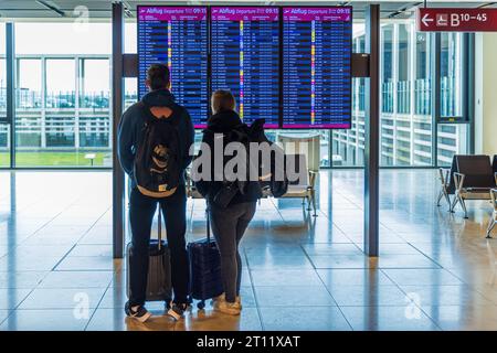 BERLINO, GERMANIA - 9 OTTOBRE 2023: Giovani coppie al display informazioni sulla partenza alla ricerca del loro volo. Foto Stock