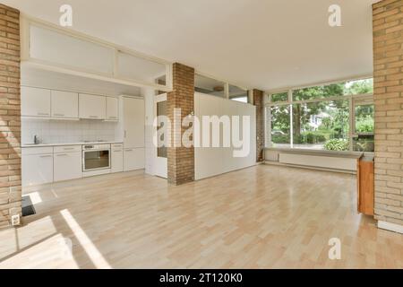un soggiorno vuoto con pavimenti in legno ed elettrodomestici bianchi è ben illuminato dal sole che splende attraverso le finestre Foto Stock