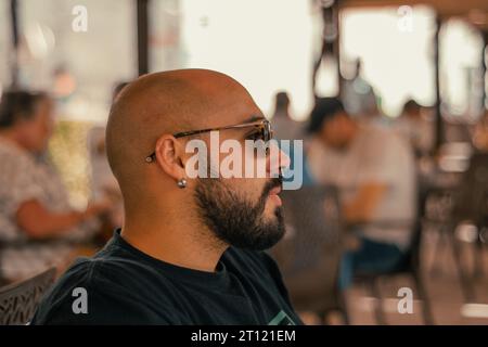 Uomo seduto su una terrazza a Granada, in Spagna, che indossa una camicia nera, occhiali da sole e piercing. Foto Stock