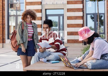 Gruppo multietnico di tre studenti universitari che fanno i compiti insieme all'aperto nel campus Foto Stock