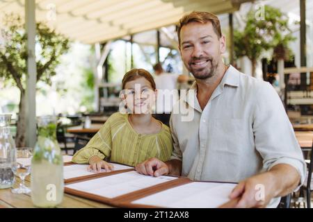 Padre e figlia leggono i menu in un ristorante, scegliendo cibo e bevande. Foto Stock