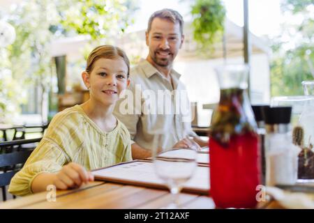 Padre e figlia leggono i menu in un ristorante, scegliendo cibo e bevande. Foto Stock