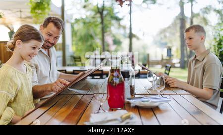 Padre e bambini leggono i menu in un ristorante, scegliendo cibo e bevande. Foto Stock