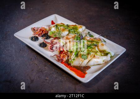 Calamari fritti con salsa su fondo nero, su un piatto bianco Foto Stock