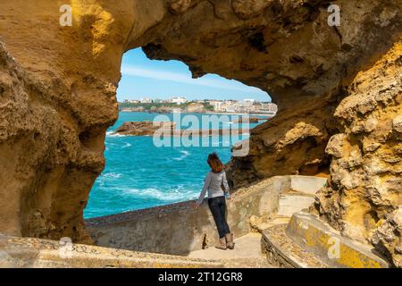 Una giovane donna che guarda in una finestra sulle rocce vicino a Plage du Port Vieux a Biarritz, in vacanza nel sud-est della Francia. Biarritz, dipartimento di Foto Stock