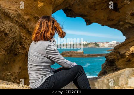 Una giovane donna che guarda in una finestra sulle rocce vicino a Plage du Port Vieux a Biarritz, in vacanza nel sud-est della Francia. Biarritz, dipartimento di Foto Stock