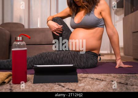 Dettaglio di una giovane donna caucasica incinta con t-shirt grigia che esegue l'esercizio di pilates. Esercizi online in classi preparatorie, benessere durante Foto Stock