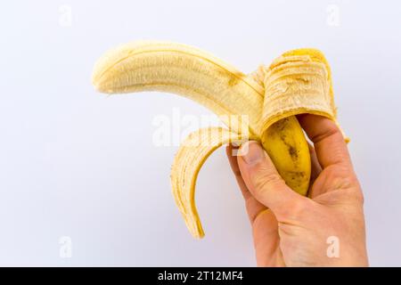 Una banana sbucciata nella mano di una donna su uno sfondo bianco Foto Stock