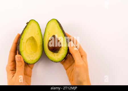 Mani di una donna che separa l'avocado in due con spazio per copiare e incollare. Ricetta per preparare un bel guacamole Foto Stock