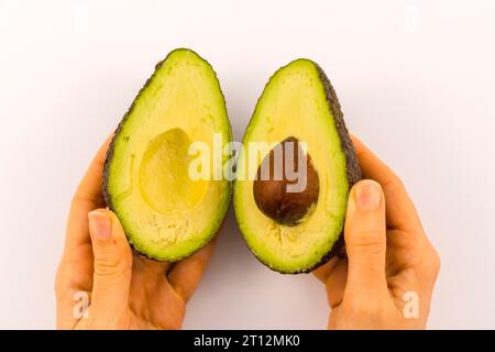 Mani di una donna che separa l'avocado in due con spazio per copiare e incollare. Ricetta per preparare un bel guacamole Foto Stock