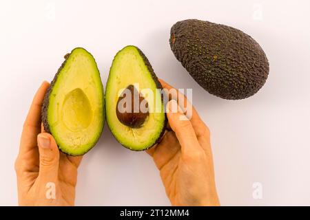 Le mani di una donna che separa l'avocado in due e uno senza taglio. Ricetta per preparare un bel guacamole Foto Stock