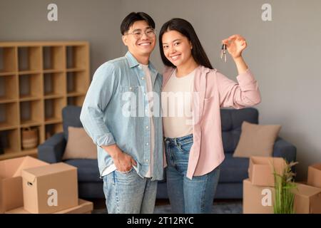 Gioiosa coppia cinese che tiene le chiavi di casa tra scatole mobili al coperto Foto Stock