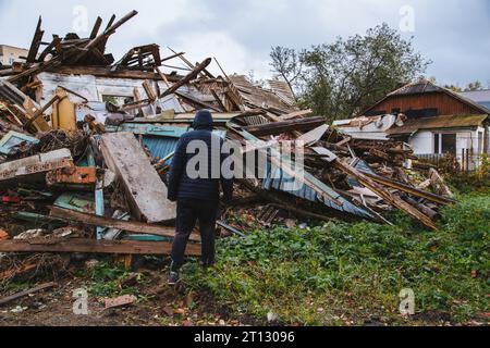 Un uomo triste in una casa in rovina. Senza speranza, senzatetto, risultato di conflitti militari e calamità naturali concetto. Foto Stock