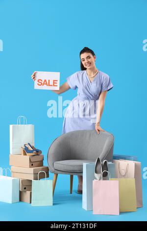 Venditore femminile con segno di vendita, scatole di scarpe, borse per la spesa e poltrona su sfondo blu Foto Stock