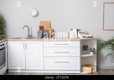 Banchi da cucina bianchi con tagliere, portapiastre, lavandino e utensili Foto Stock