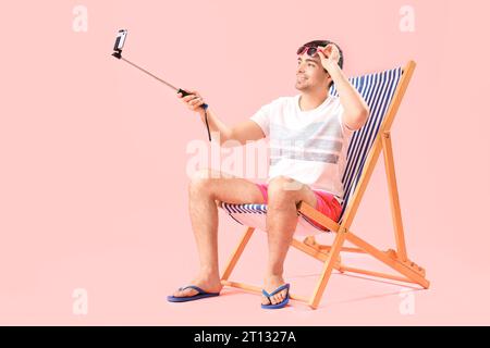 Giovane che scatta selfie su una sedia a sdraio su sfondo rosa Foto Stock
