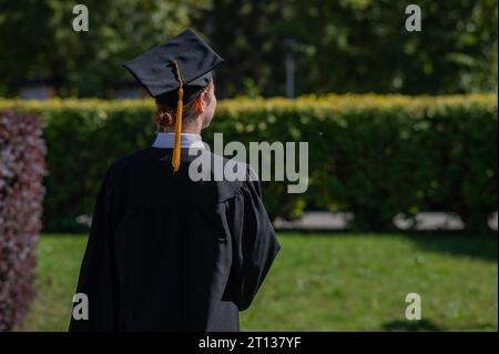 Una donna lancia il suo cappellino di laurea contro il cielo blu. Foto Stock