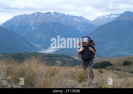 Tramper che trasporta un grande branco cammina in salita sulle montagne delle alpi meridionali della nuova Zelanda Foto Stock