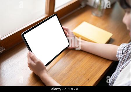 L'immagine ravvicinata di un tablet mockup con schermo bianco è nelle mani di una donna. Una donna che usa il suo tablet digitale a un tavolo in un bar. Persone e tecnologia con Foto Stock