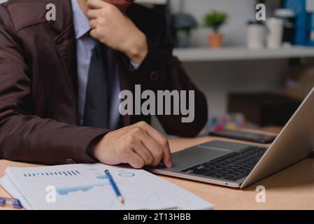 Uomo d'affari che digita la tastiera mentre lavora alla scrivania. Report aziendali che analizzano grafici finanziari e di marketing documentano e documentano l'analisi dei dati Foto Stock