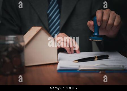 agente immobiliare con casa. Persona d'affari in possesso di un timbro di gomma approvato sul contratto di mutuo ipotecario piano dell'abitazione sulla tabella. Foto Stock