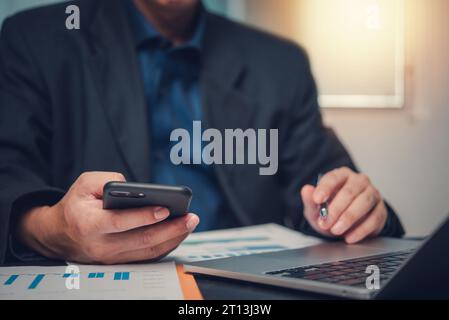 Uomo d'affari che analizza i dati su laptop e grafico per la pianificazione finanziaria, segnala il marketing su scrivania. Foto Stock