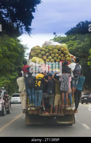 Cagayan de Oro, Filippine: Le persone si aggrappano al retro di una jeepney in movimento, piena di frutta, sacchi di verdura, casse di birra. Trasporti pubblici. Foto Stock