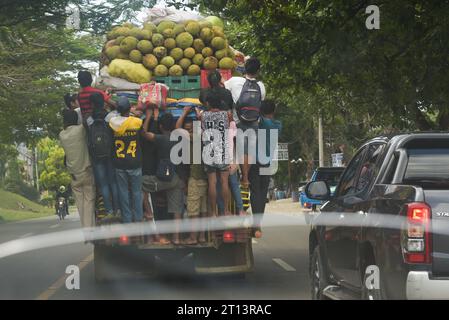 Cagayan de Oro, Filippine: I pendolari filippini si aggrappano al retro di una jeepney in movimento, piena di frutta e sacchi di verdura. Paese del terzo mondo. Foto Stock