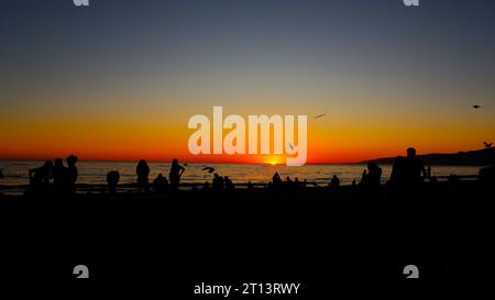 Suggestivo tramonto sulla spiaggia con sagome di persone che guardano il tramonto Foto Stock