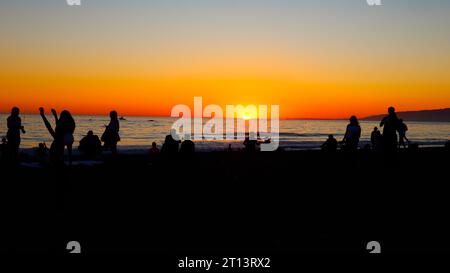 Suggestivo tramonto sulla spiaggia con sagome di persone che guardano il tramonto Foto Stock