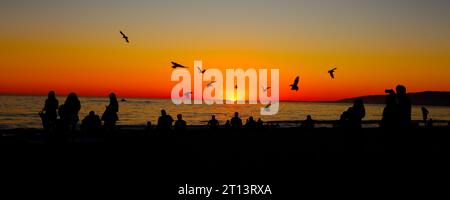 Suggestivo tramonto sulla spiaggia con sagome di persone che guardano il tramonto Foto Stock