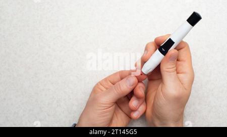 L'uomo caucasico di mezza età si è forato il dito per la vista piatta del test del glucosio a casa Foto Stock