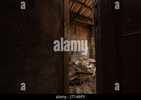 Una porta di legno aperta a metà porta alla stanza distrutta dagli agenti atmosferici di un edificio abbandonato alla luce del giorno Foto Stock