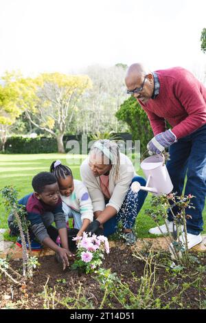 Felici nonni e nipoti afroamericani che annaffiano le piante in un giardino soleggiato Foto Stock