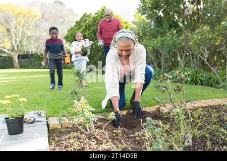 Felici nonni e nipoti afroamericani che piantano piante in un giardino soleggiato Foto Stock