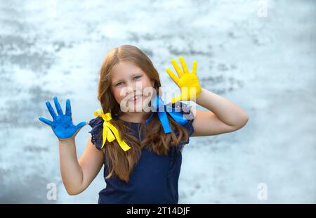 Ragazza felice che mostra i palmi delle mani dipinti in giallo e blu. Indipendenza, bandiera. Giorno della costituzione dell'Ucraina. Educazione, scuola, arte e concetto di pittura Foto Stock