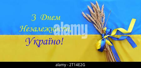 Un bouquet di spikelets dorati e maturi di grano legati con un nastro giallo e blu sullo sfondo della bandiera Ucraina. L'iscrizione in ucraino Foto Stock
